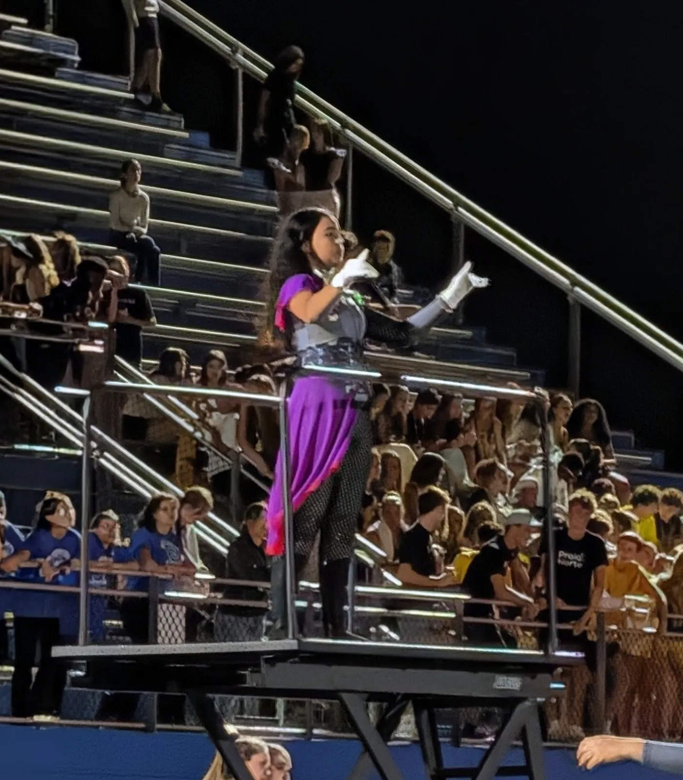 The drum major conducting the Wilson Warrior Marching Band from the podium, the home stands full behind her