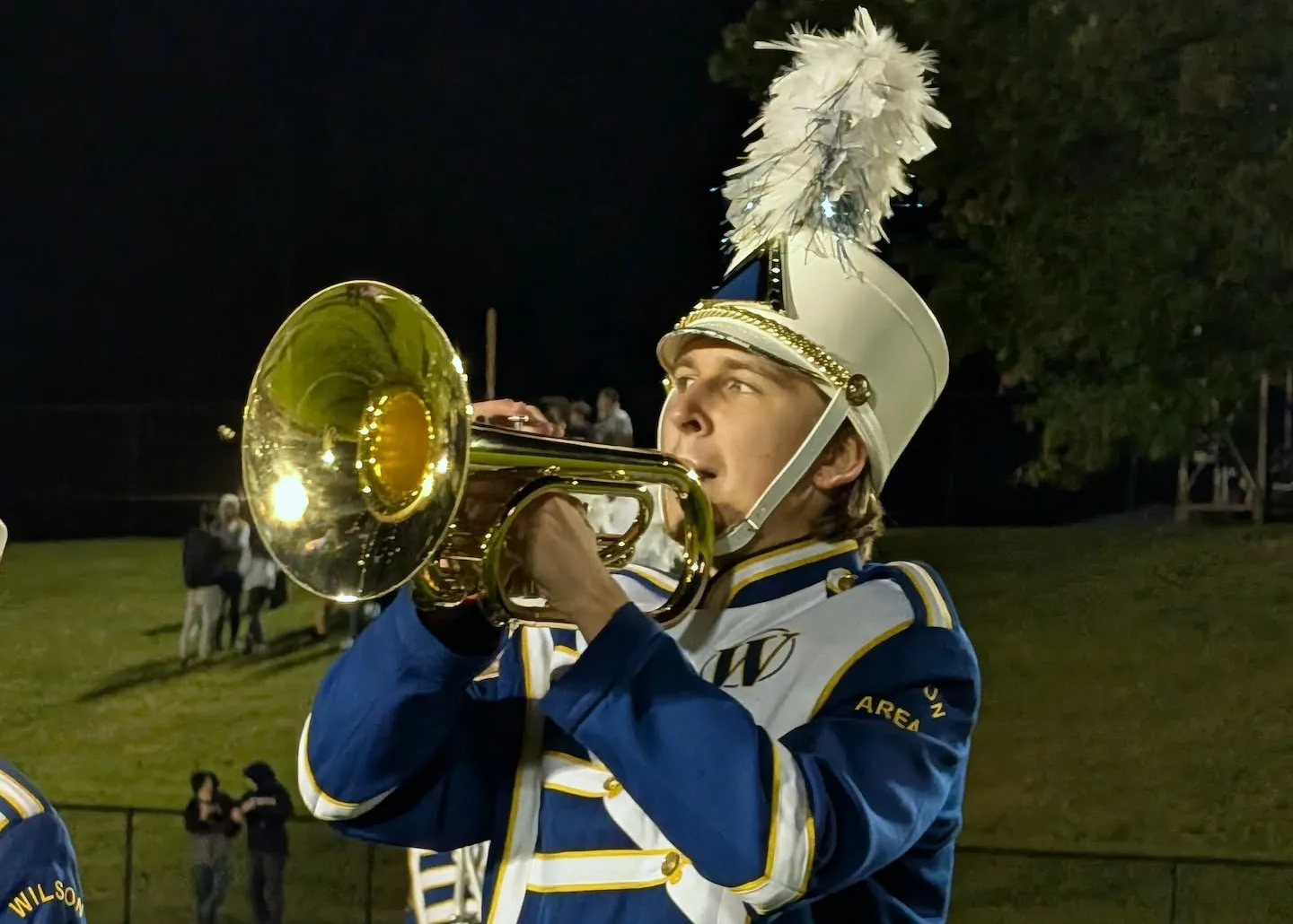 A mellophone player in full uniform and plumed shako, playing on the field